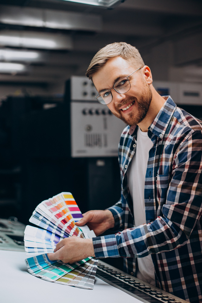 Graphic designer holding color swatches while preparing print materials in a professional printing studio